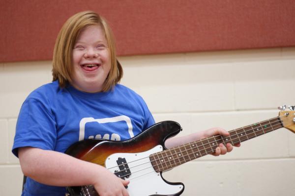 An IMPs member smiling and holding a guitar