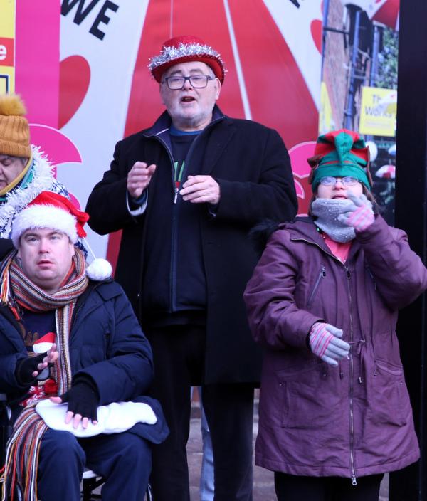 Three people sign as they sing Christmas Carols in festive Santa hats
