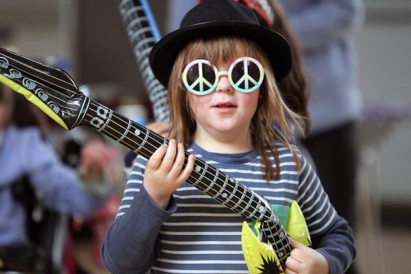 A young boy wears peace sign sunglasses and and inflatable guitar