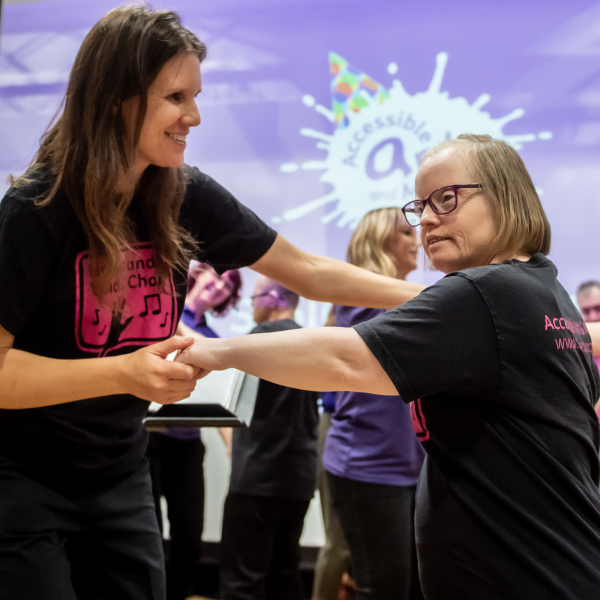 A smiling woman dances with Hands & Voices participant