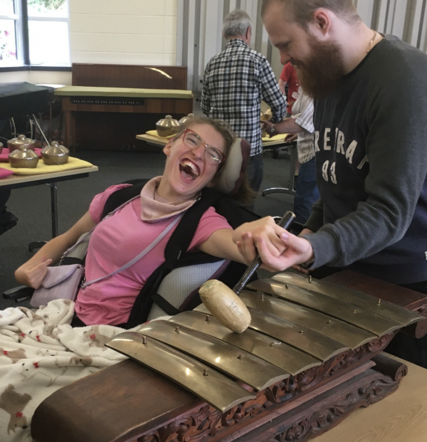 A woman wears pink and smiles as she strikes instruments with a mallet