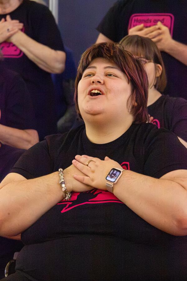 A young woman singing and smiling, with her hands on her chest