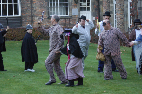 Performers dressed as cops, robbers and Laurel and Hardy chase each other 